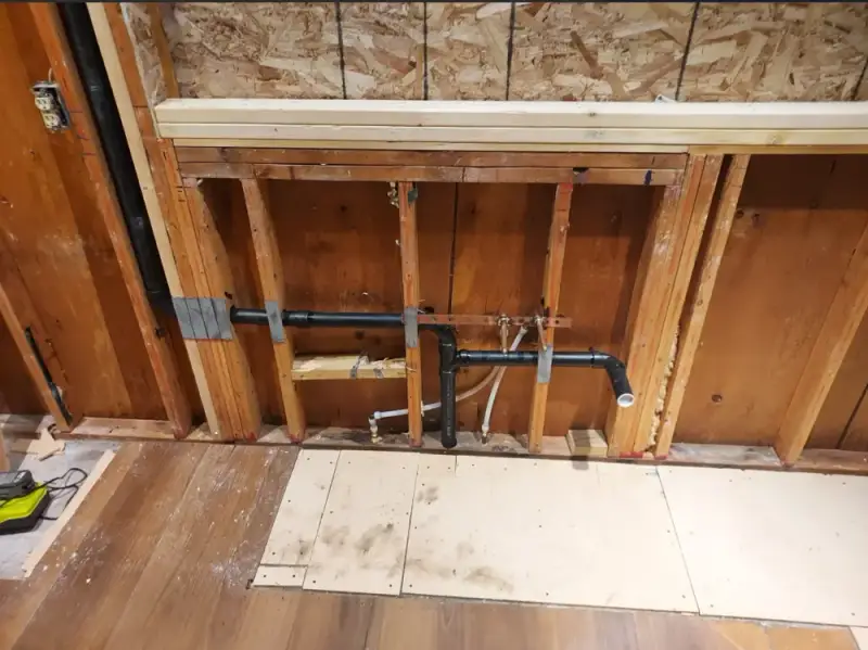 Copper and ABS pipes re-routed inside a wood-framed wall during a pipe repair