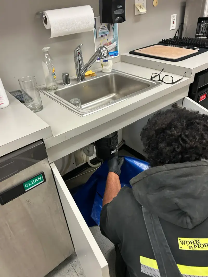Technician installing a new garbage disposal under a commercial breakroom sink