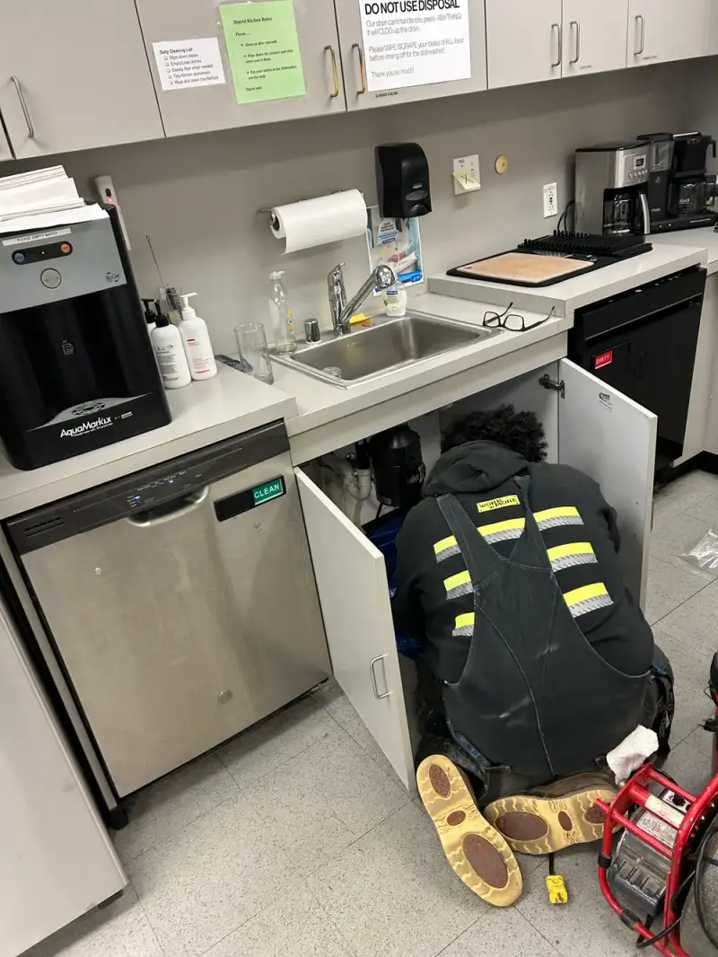 Plumber repairing a drain inside the sink cabinet of a commercial breakroom