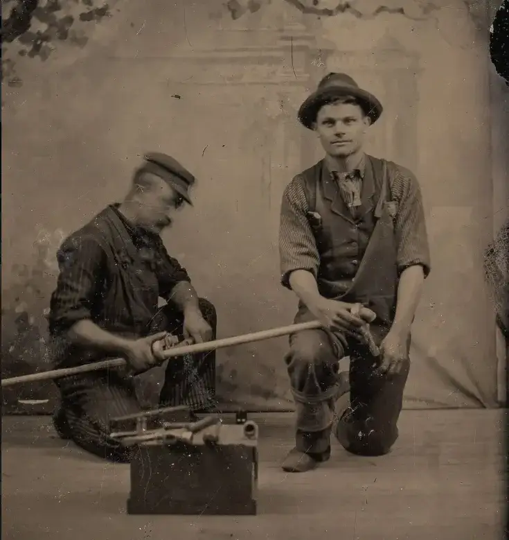 Vintage photograph of two early-1900s plumbers posing with pipe and threading tools